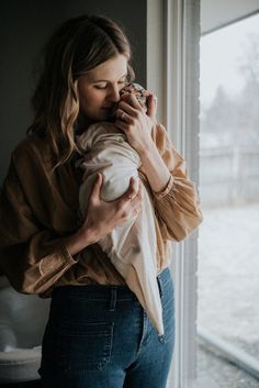 a woman holding a baby in her arms and looking out the window with snow outside