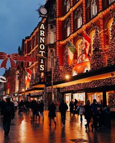 people walking down the street in front of buildings decorated with christmas lights and garlands