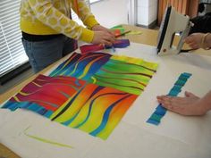 two women working on art work at a table with paper and scissors in front of them