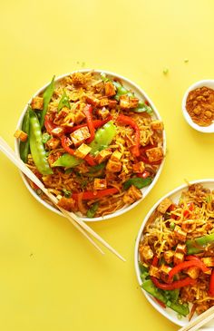 two bowls filled with food next to chopsticks and seasoning on a yellow surface