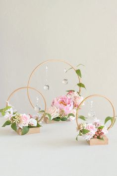 pink flowers and greenery are arranged in gold hoop vases on a white surface