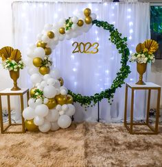 the balloon arch is decorated with white and gold balloons, greenery, and golden vases