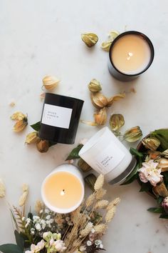 two candles sitting on top of a table next to some flowers and leaves with one candle in the middle