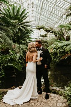 a bride and groom standing in front of a pond surrounded by greenery at their wedding