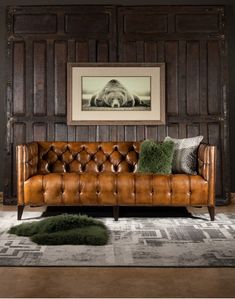 a leather couch in front of a wooden paneled wall with a framed photo on it