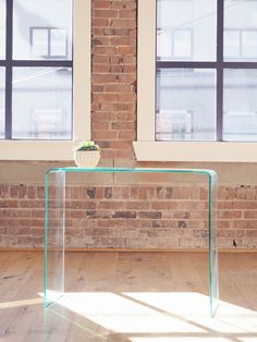 a clear glass table sitting on top of a hard wood floor next to two windows