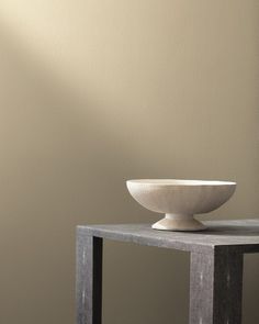 a white bowl sitting on top of a wooden table next to a gray wall in a room