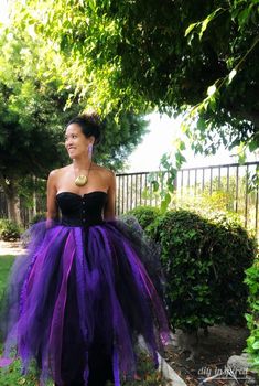 a woman wearing a purple and black dress standing in the grass with her hands on her hips