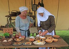 two women are standing at a table with food on it