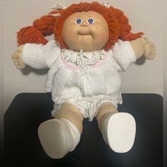 a doll with red hair and blue eyes sitting on top of a black table next to a white wall