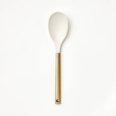 a white and gold spoon sitting on top of a white table next to a yellow handle