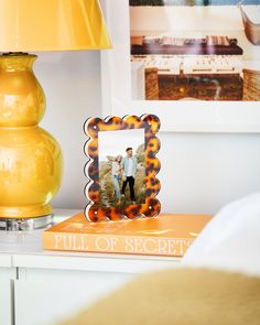 an orange lamp on top of a white table next to a yellow book and photo frame