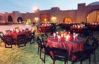 an outdoor dining area with red tablecloths and black chairs, lit by candles