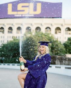 a woman in a graduation gown is holding a bottle and spraying water on her face