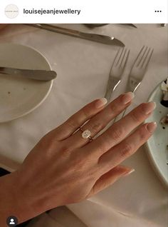 a woman's hand with a diamond ring on top of her finger next to a plate of food