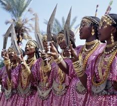 a group of women dressed in pink and gold holding up some large knife's