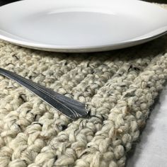 a white plate sitting on top of a crocheted table cloth next to a fork