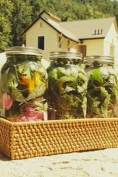 four mason jars filled with flowers sitting on top of a wooden basket next to a building