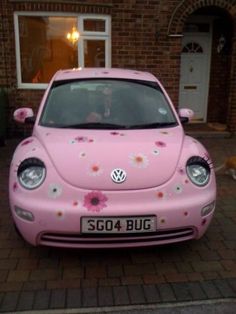 a pink vw bug parked in front of a brick house with flowers painted on it