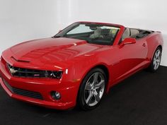 a red chevrolet camaro convertible is parked in a white room with black carpeting