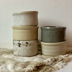 three ceramic cups sitting next to each other on top of a cloth covered tablecloth