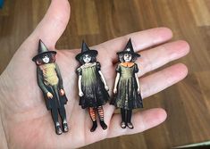 three small dolls are sitting on the palm of someone's hand, one is wearing a witch hat