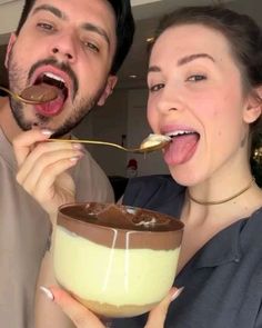 a man and woman eating chocolate from a bowl with spoons in their mouths while posing for the camera