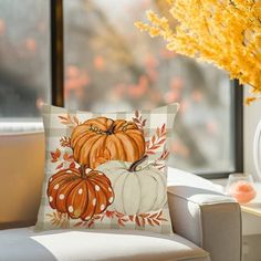 a couch with a pillow on it next to a vase filled with flowers and pumpkins