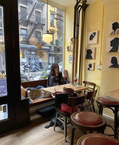 a woman sitting at a table in front of a window with pictures on the wall