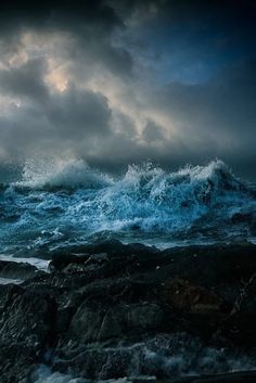 an ocean scene with waves crashing on the rocks and dark clouds in the sky above