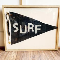 a framed surf sign sitting on top of a wooden floor next to a white wall