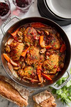 a pan filled with meat and vegetables on top of a table next to some bread