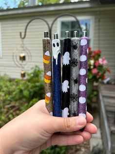 a hand holding four different colored lighters in front of a house with halloween decorations on them