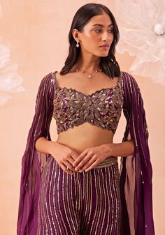 This exquisite Wine Embroidered Pant set, crafted from luxurious silk organza, perfectly blends traditional charm and contemporary style. The wine-hued blouse is adorned with intricate zari and sequin work, with detailed cutwork on the neckline adding a touch of sophistication. The long, soft cape sleeves elevate the ensemble, infusing it with a graceful and modern twist. The matching sharara pants are gracefully embellished, creating a stunning vibe. Perfect for Cocktail, Sangeet ceremonies or as a wedding guest. Composition : Pant & Blouse : Silk Organza Care: Dry Clean Only and Vacuum Storage This product can be customized for sleeves, length and colour Delivery : 4-6 weeks as the product is hand crafted. Check Size Guide or choose MySize for free customisation (All Sizes above XL can b Traditional Silk Palazzo Set With Sequins, Purple Silk Sets For Reception, Bollywood Style Purple Palazzo Set With Intricate Embroidery, Glamorous Organza Sets, Silk Palazzo Set With Sequins For Reception, Bollywood Style Purple Embroidered Palazzo Set, Purple Sequined Sets For Eid, Eid Sequinned Purple Sets, Eid Purple Sequin Sets