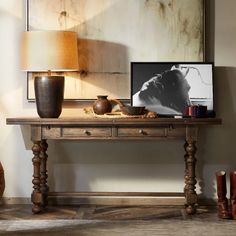 a wooden table topped with a lamp next to a painting and vase on top of it