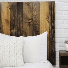 a bed with white sheets and pillows against a wooden headboard in front of a brick wall