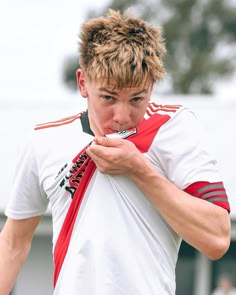 a young man holding a toothbrush in his mouth while wearing a red and white shirt