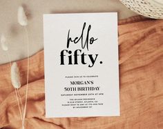 a card with the words hello fifty on it sitting on top of a bed next to some feathers