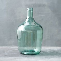 an empty green glass bottle sitting on top of a cement floor next to a gray wall