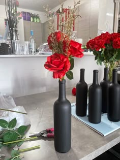 three black vases with red roses in them on a counter top next to flowers