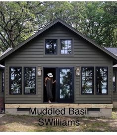 a woman standing in the open door of a small house with muddled basill sidings