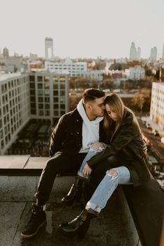 a man and woman sitting on top of a building next to each other with buildings in the background