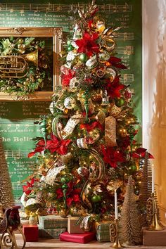 a christmas tree decorated with red, gold and silver ornaments in front of a green wall