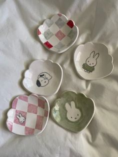 four small plates with designs on them sitting on a white sheet in the shape of hearts