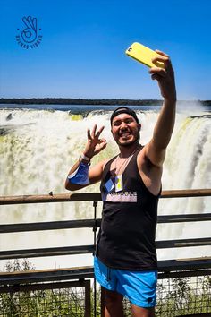 a man standing in front of a waterfall with his hand up and the water falling behind him