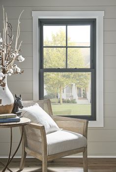 a living room with a chair, table and vase filled with flowers next to a window