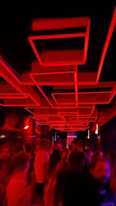 a group of people standing around in a room with red lights on the ceiling and floor