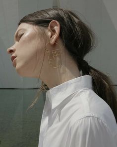 a woman with long hair wearing large gold earrings and a white shirt is looking off into the distance