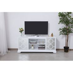 a white entertainment center with a flat screen tv on it's stand and potted plant in the corner