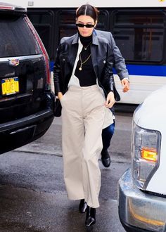 a woman in black jacket and pants walking next to a bus